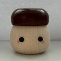 A small wooden acorn-shaped container or figurine with a smooth dark brown cap, natural light wood body, painted black eyes, and pink cheeks, centered against a plain light gray background.