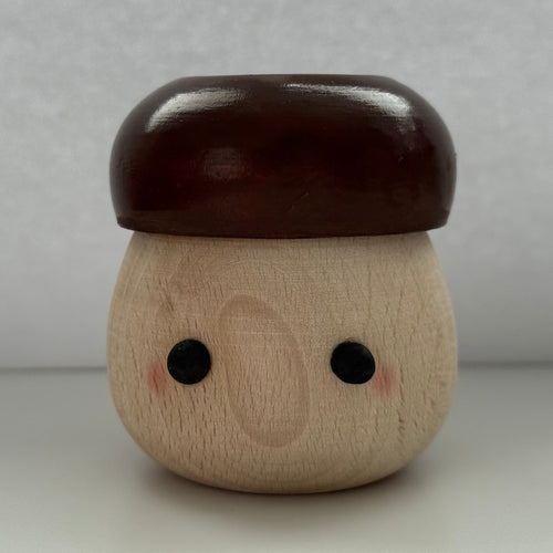 A small wooden acorn-shaped figurine with a glossy dark brown cap and a natural light wood body featuring simple black eyes and pink cheeks, set against a neutral gray background.